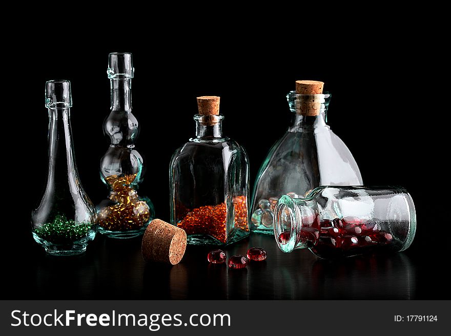 Glass bottles filled with colorful beads on a black background. Glass bottles filled with colorful beads on a black background.
