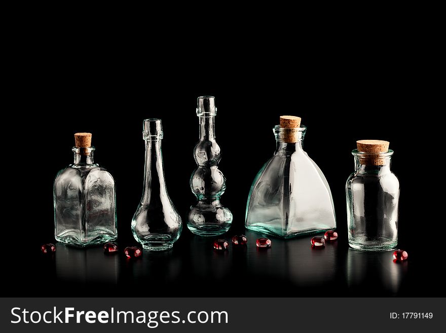 Several small, empty green glass bottles - some with stoppers, with red glass pebbles on a black background.