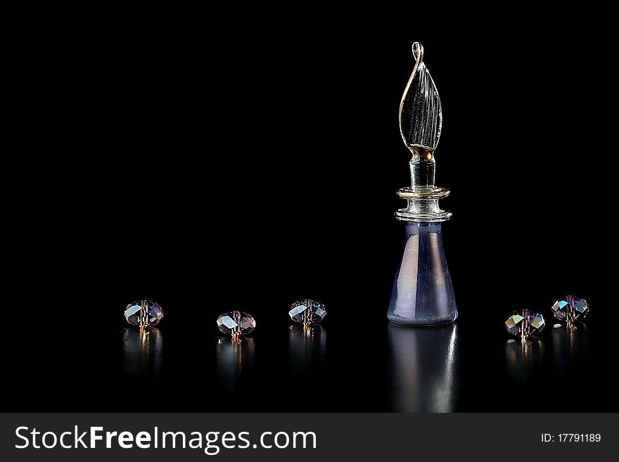 A purple perfume bottle and crystal beads on a black background. A purple perfume bottle and crystal beads on a black background.