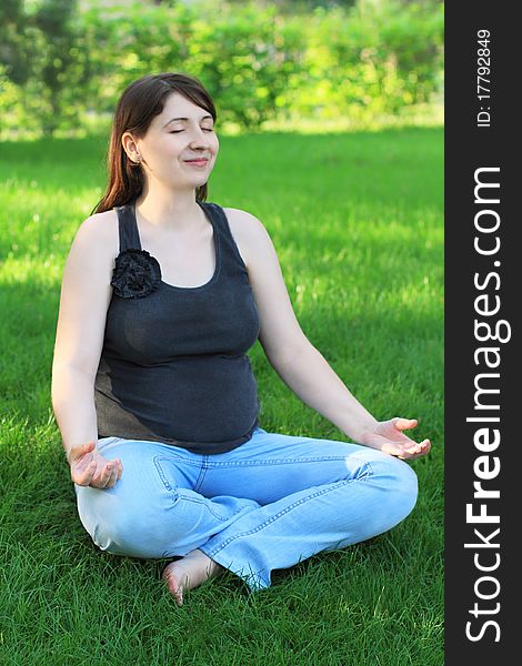 Pregnant woman sits on grass doing yoga. Pregnant woman sits on grass doing yoga