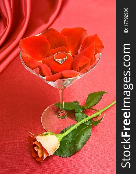 Petals and the ring in the glass for Martini. Rose on the red background. Petals and the ring in the glass for Martini. Rose on the red background.