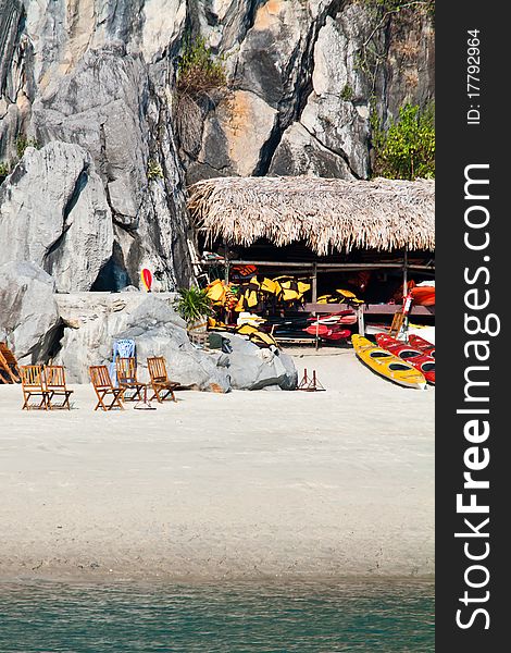 Beach and island in a remote area of Halong bay. Kayaks and deck chairs lying on the beach in the background there is a steep cliff. Beach and island in a remote area of Halong bay. Kayaks and deck chairs lying on the beach in the background there is a steep cliff