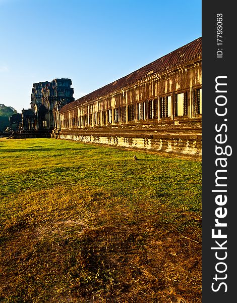 Large outer wall of the ruined temple Angkor Wat in the early morning sun. Golden colours and grass leading up to a stone structure. Large outer wall of the ruined temple Angkor Wat in the early morning sun. Golden colours and grass leading up to a stone structure