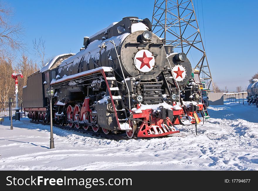 Steam locomotive beside a railway station platform. Winter. Retro train.