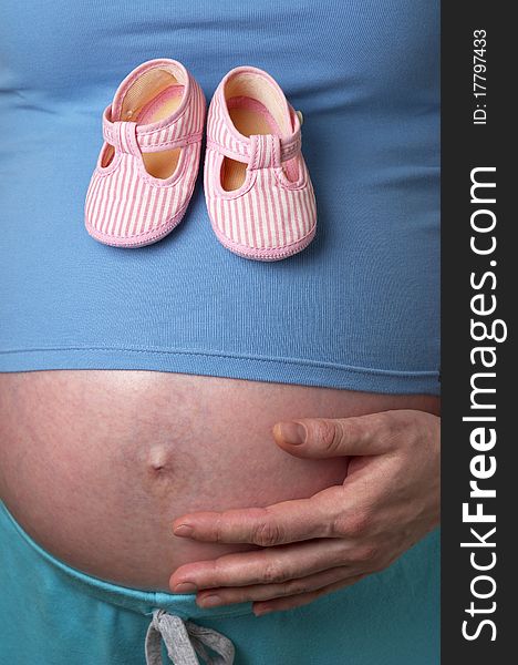 Pregnant woman profile with tiny shoes in the hands over white background. Pregnant woman profile with tiny shoes in the hands over white background