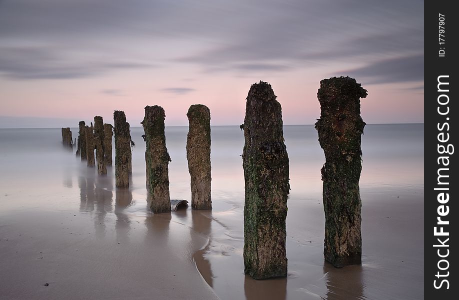 An abandoned series of posts jut out into the sea as the waves and tides pass by. An abandoned series of posts jut out into the sea as the waves and tides pass by.