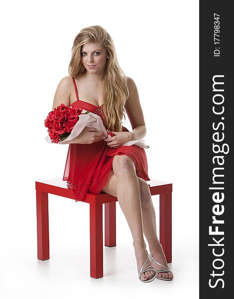 Attractive teenage girl in a red dress holding a bouquet of roses sitting on red table. Attractive teenage girl in a red dress holding a bouquet of roses sitting on red table