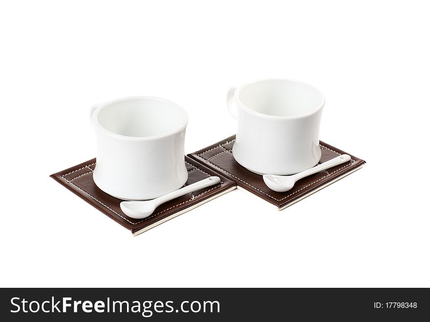 Two empty tea cups with spoons on table mats. Isolated on white background. Two empty tea cups with spoons on table mats. Isolated on white background.