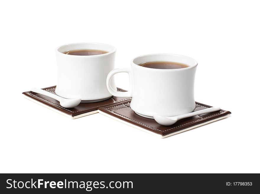 Two cups with tea, two spons on table mats. Isolated on white backgrond. Two cups with tea, two spons on table mats. Isolated on white backgrond.