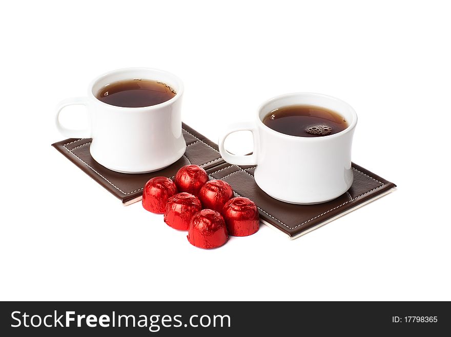Two cups with tea on table mat and sweets. Isolated on white background. Two cups with tea on table mat and sweets. Isolated on white background.