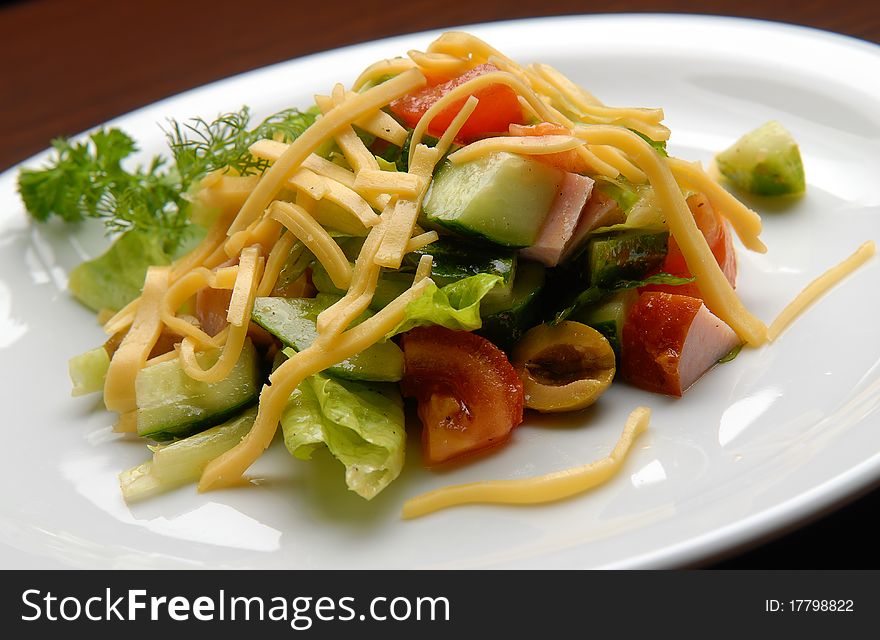 Salad with fresh vegetables and cheese, ham and olives on a plate