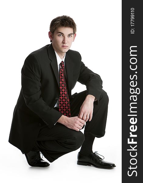 Attractive teenage boy kneeling in a suit isolated on white background