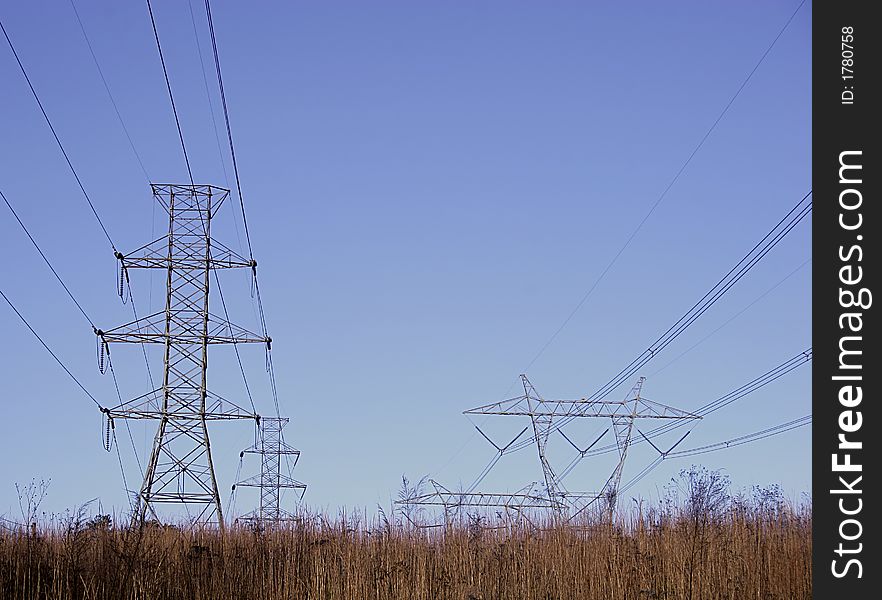 Open grass field with high power electrical pylons and blue sky. Open grass field with high power electrical pylons and blue sky