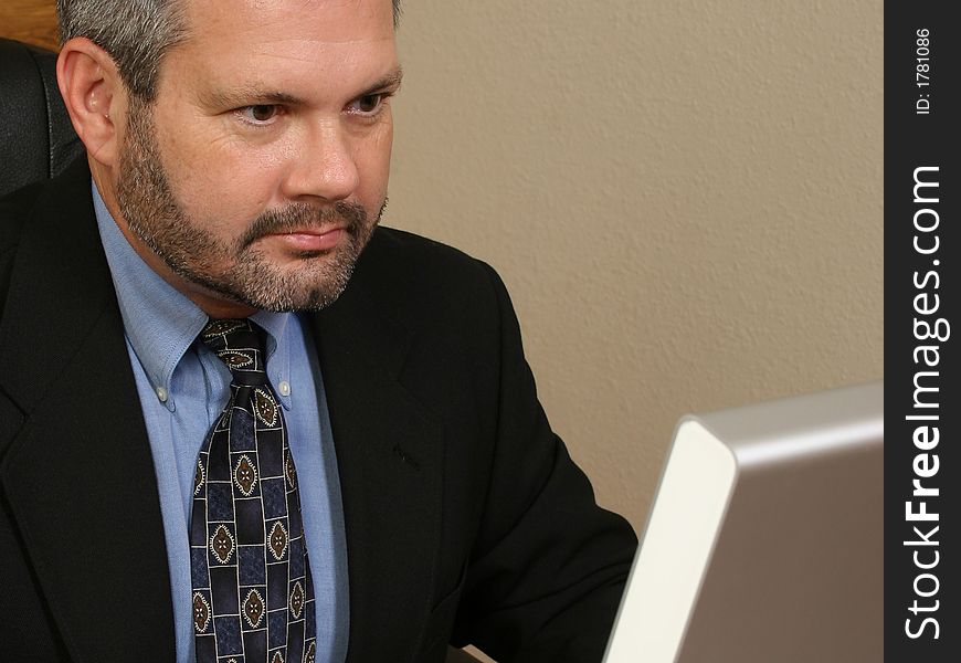 Fourty something business man in suit sitting at desk looking at monitor. Fourty something business man in suit sitting at desk looking at monitor.