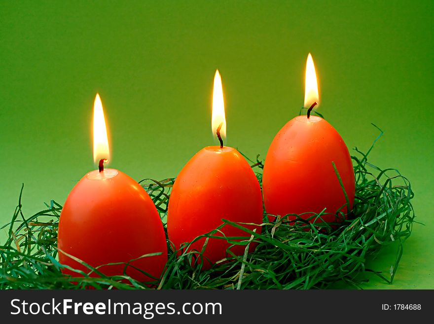 Three egg candles in orange with easter grass on green. Three egg candles in orange with easter grass on green