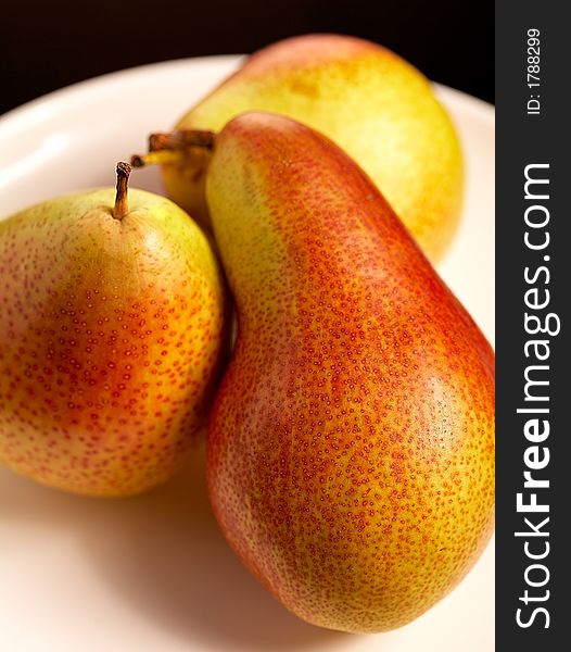 Three pears on white plate on black background