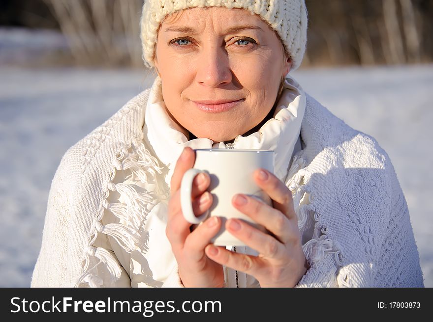 Adult woman in white, with mug in his hands  on a snowy background, bright sunny frosty day