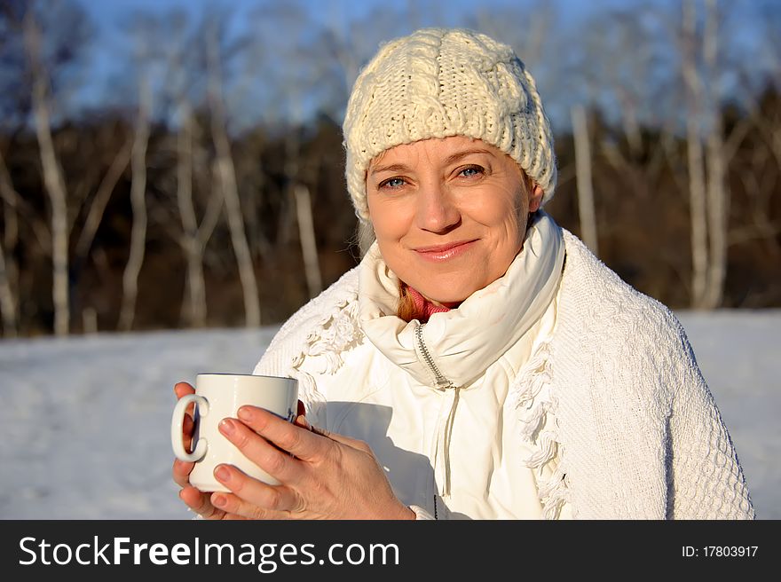 Adult woman in white, with mug in his hands  on a snowy background, bright sunny frosty day