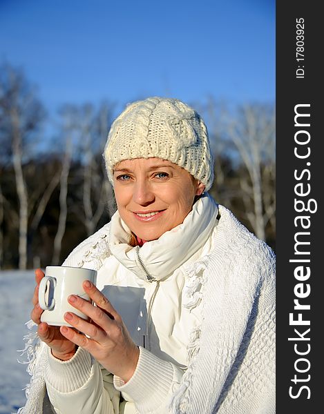 Adult woman in white, with mug in his hands  on a snowy background, bright sunny frosty day