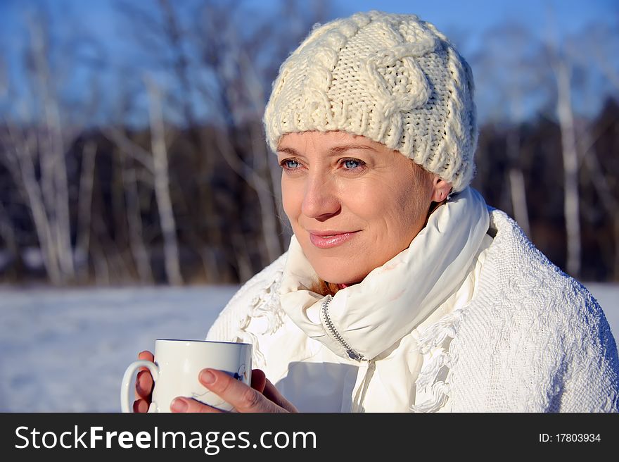 Adult woman in white, with mug in his hands  on a snowy background, bright sunny frosty day