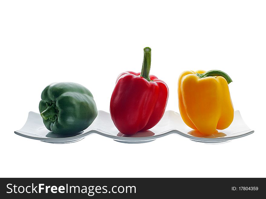 One red, one yellow and one green pepper on white dish. One red, one yellow and one green pepper on white dish