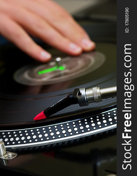 Focus is on the needle and the hand of a disc jockey is on the background. Focus is on the needle and the hand of a disc jockey is on the background