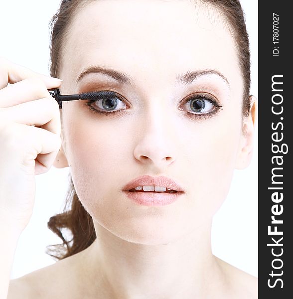 Portrait of pretty young woman applying mascara using lash brush