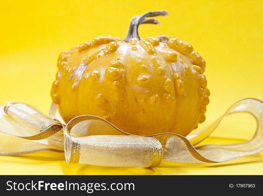 Yeallow pumpkin on yellow background with golden ribbon for hellowen or for a gift