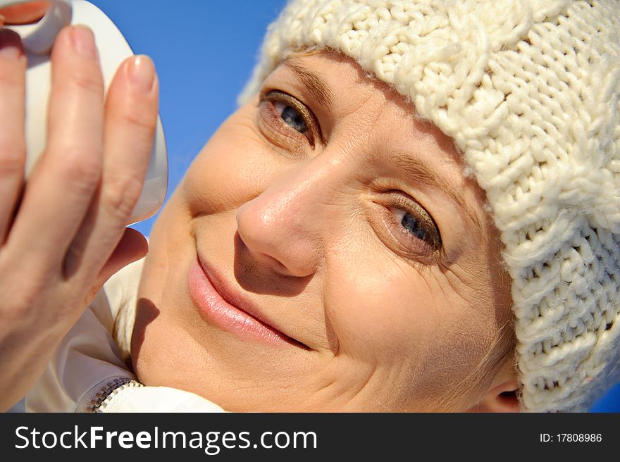 Portrait of adult woman in white, with mug in his hands, bright sunny frosty day