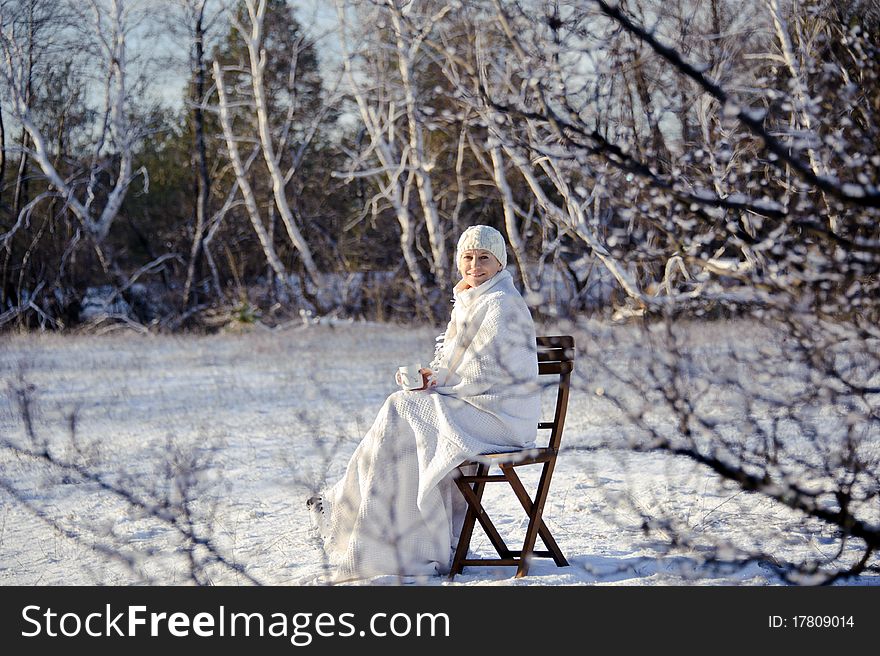 Adult woman in white, with mug in his hands  on a snowy forest background, bright sunny frosty day. Adult woman in white, with mug in his hands  on a snowy forest background, bright sunny frosty day