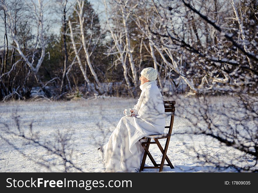 Adult woman in white, with mug in his hands on a snowy forest background, bright sunny frosty day. Adult woman in white, with mug in his hands on a snowy forest background, bright sunny frosty day