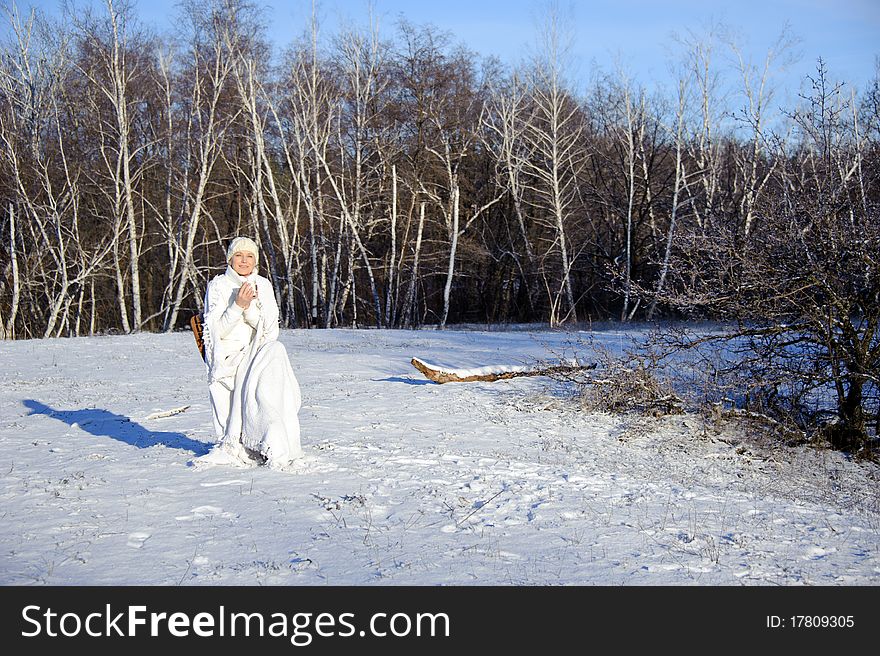 Adult woman in white, with mug in his hands on a snowy forest background, bright sunny frosty day. Adult woman in white, with mug in his hands on a snowy forest background, bright sunny frosty day.