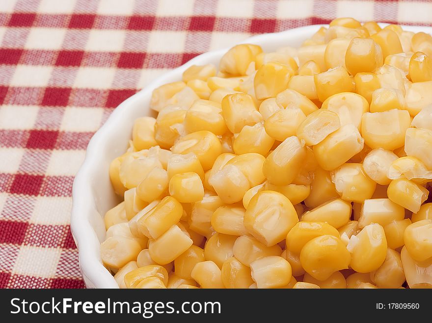 Canned corn in a white bowl on a checkered tablecloth