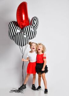 Two Happy Laughing Singing Kids Girls In Skirts And T-shirts With Air Balloons Stand Together Hugging Royalty Free Stock Images