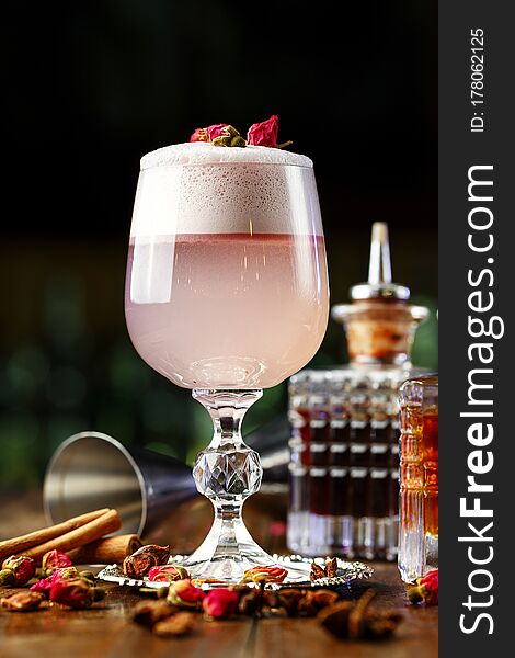 Female pink cocktail with foam in a glass. decorated with dried rose. in the background is visible barman inventory. Female pink cocktail with foam in a glass. decorated with dried rose. in the background is visible barman inventory