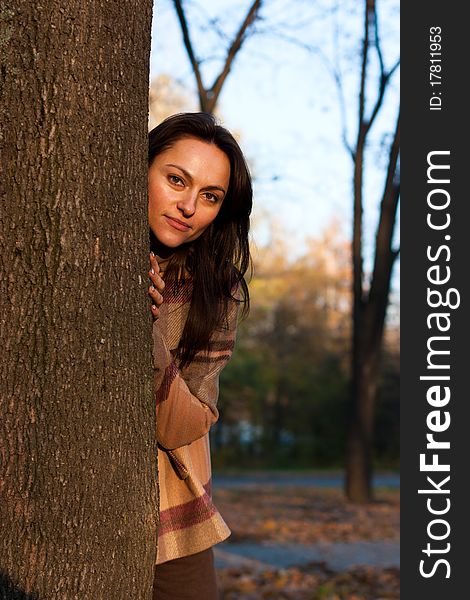 Beautiful young woman looking out behind the tree in autumn. Beautiful young woman looking out behind the tree in autumn
