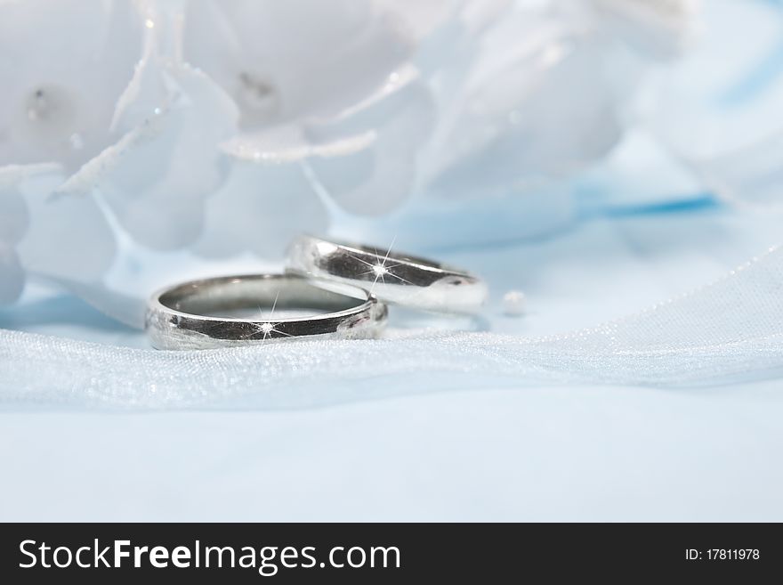 White flowers from a wedding on blue background with blue and white ribbon and two rings. White flowers from a wedding on blue background with blue and white ribbon and two rings