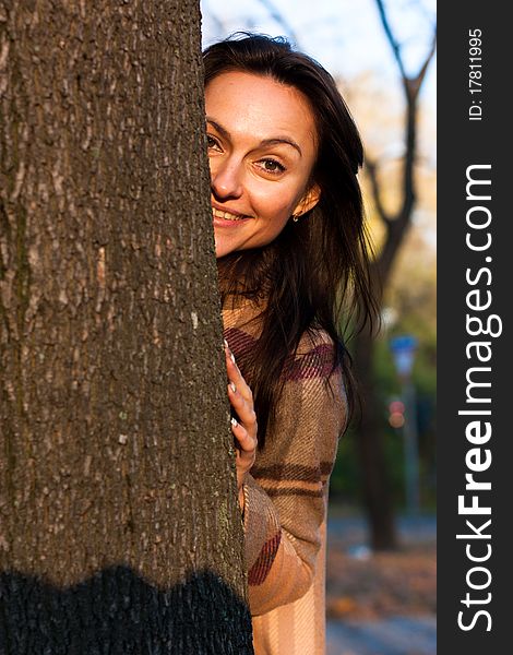 Beautiful young woman looking out behind the tree in autumn. Beautiful young woman looking out behind the tree in autumn