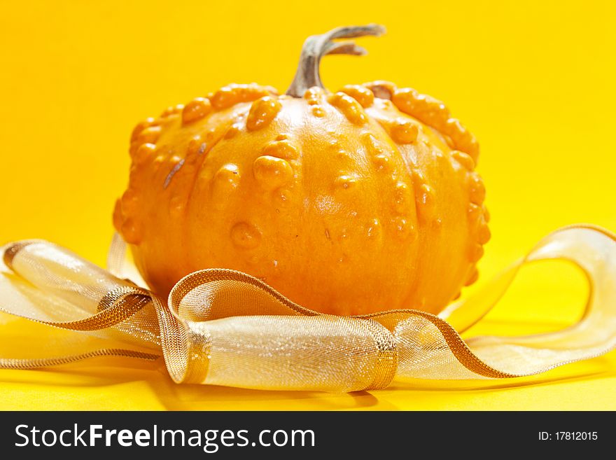 Yeallow pumpkin on yellow background with golden ribbon for hellowen or for a gift