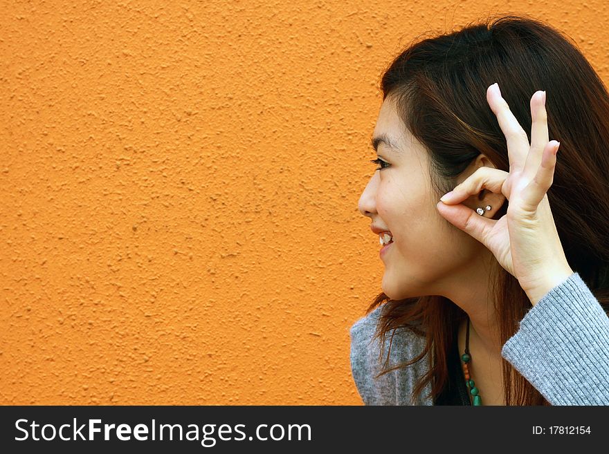 She is an Asian and trying to use her hands to pretend listening to the others. It was taken in an orange background. She is an Asian and trying to use her hands to pretend listening to the others. It was taken in an orange background.