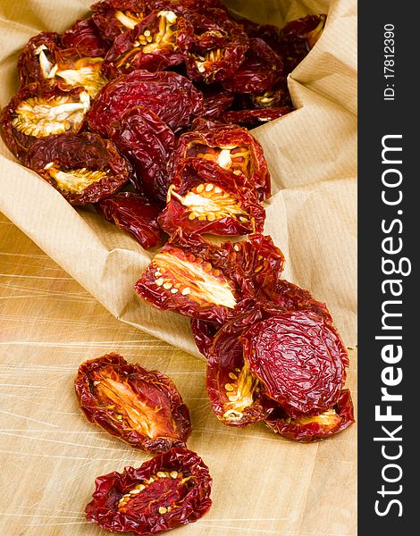 Ripe red sun-dried plum tomatoes spilling out of a brown recycled brown paper shopping bag onto a wooden cutting board surface. Ripe red sun-dried plum tomatoes spilling out of a brown recycled brown paper shopping bag onto a wooden cutting board surface