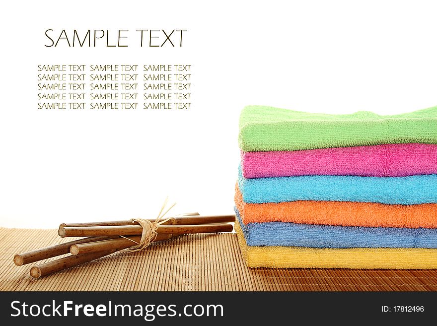 Lots of colorful bath towels stacked on each other. Side by side on a wooden surface lie bamboo sticks. Isolated