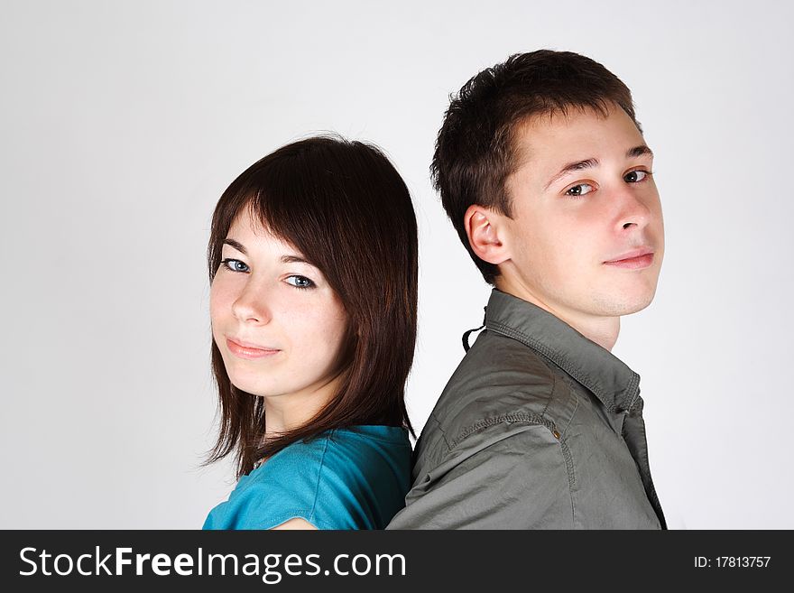 Portrait of young brunette girl and man standing back to back and looking at camera