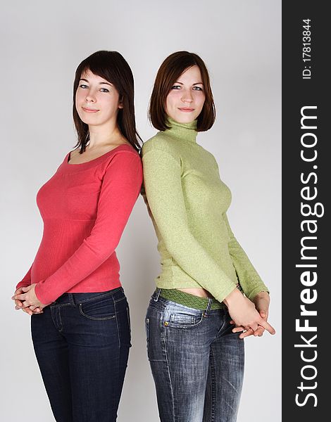 Two young brunette girls in red and green shirts standing back to back. Two young brunette girls in red and green shirts standing back to back