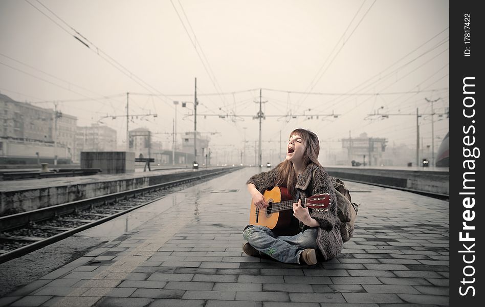 Young woman singing and playing the guitar on the platform of a train station. Young woman singing and playing the guitar on the platform of a train station