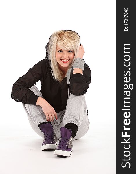 Beautiful young blonde female street dancer, wearing black and grey outfit and trainers, sitting on a white backdrop with big smile. Beautiful young blonde female street dancer, wearing black and grey outfit and trainers, sitting on a white backdrop with big smile.