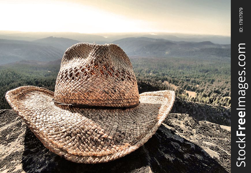 A straw cowboy hat on a high rock with forest in the background. A straw cowboy hat on a high rock with forest in the background.
