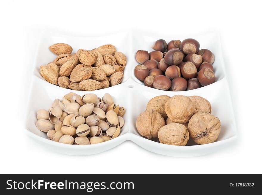 Four kinds of popular nuts lie separately in a white plate on a white background. A shot horizontal, focus in the shot center