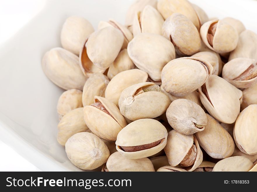Many pistachios lie on a white plate, the Shot horizontal, focus in the shot center, a background white