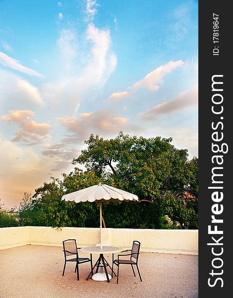 A rooftop getaway, with a table, umbrella and two chairs.  A beautiful sky and clouds are in the background. A rooftop getaway, with a table, umbrella and two chairs.  A beautiful sky and clouds are in the background.